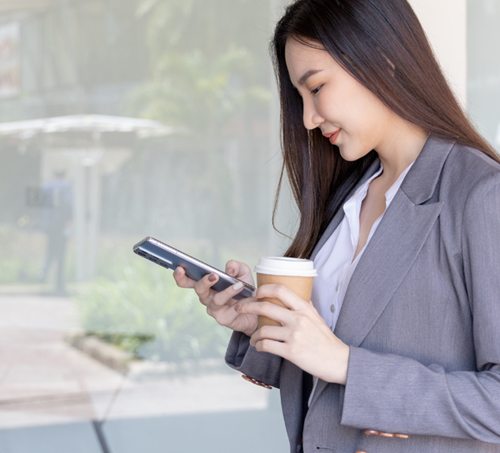 Une femme souriante tenant un smartphone et un café dans ses mains