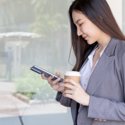 Une femme souriante tenant un smartphone et un café dans ses mains