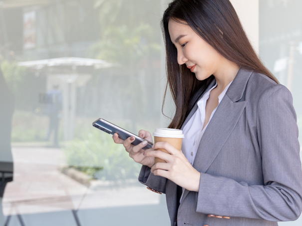 Une femme souriante tenant un smartphone et un café dans ses mains