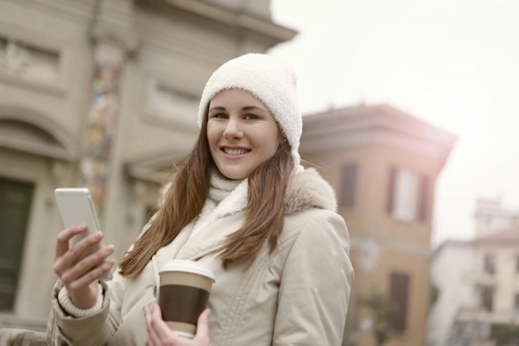 Une femme avec un bonnet et un manteau tenant son smartphone à la main