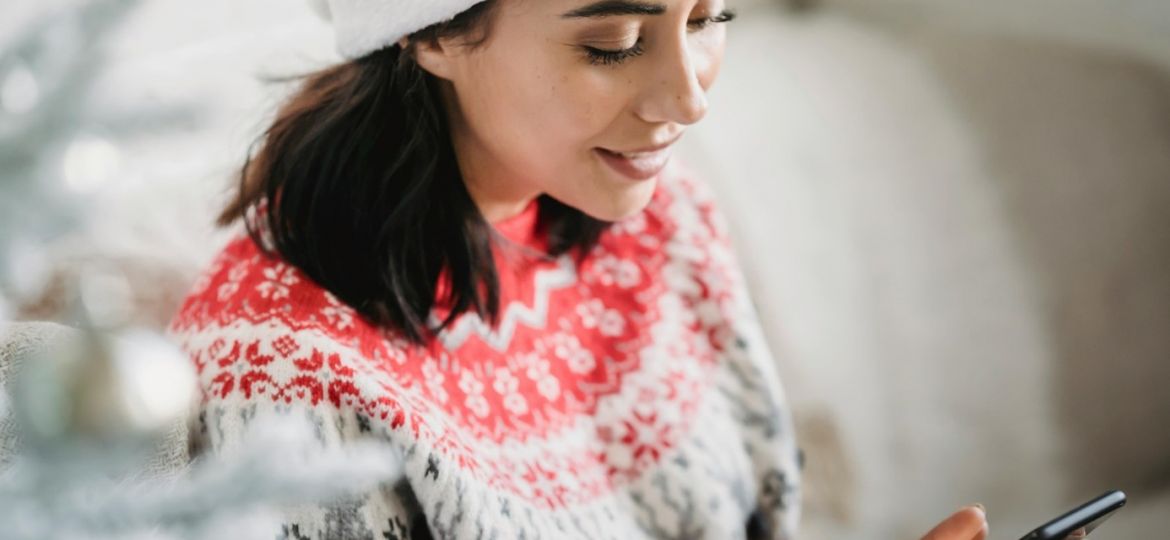 Une femme avec un pull et bonnet de Noël recevant un SMS marketing