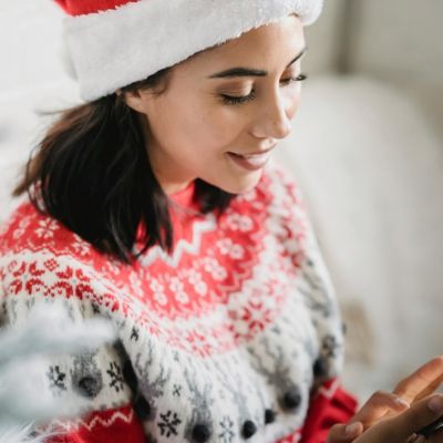 Une femme avec un pull et bonnet de Noël recevant un SMS marketing