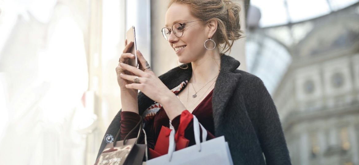 Une femme souriante faisant les soldes d’hiver, smartphone à la main